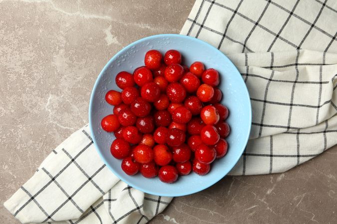 Bowl with red cherry and towel on gray background, top view
