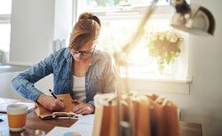 Female entrepreneur writing on bags of products while fulfilling orders from her home office