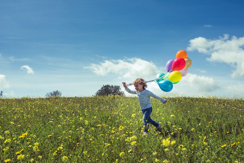 Positive boy with balloons enjoying summer in green field