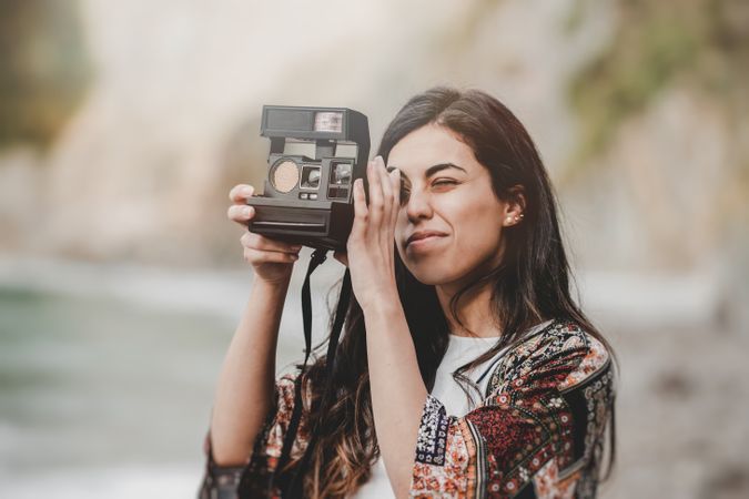 Woman with camera on shore near stones and water