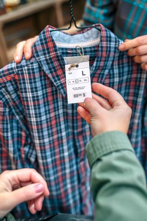 Close up of unrecognizable female customer hand holding label of plaid shirt on clothing store