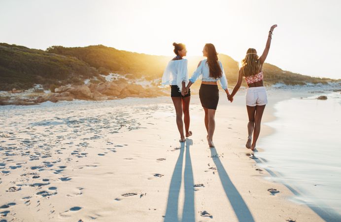 Female college students holding hands along the ocean