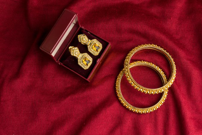 Beautiful shiny golden bangles and diamond studded traditional earrings on a red velvet background