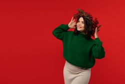 Woman in Christmas wreath looking up joyfully against red background.