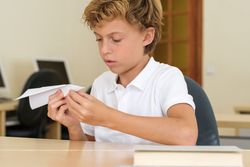 Serious boy making paper airplane at school