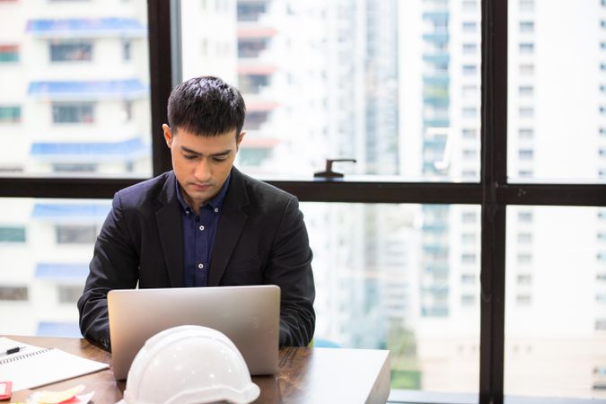 Asian male sitting and working on laptop at desk in the office