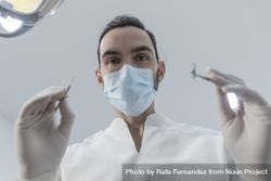 Low angle view of male dentist in medical mask holding dentist tools for dental procedure in clinic 49DXE5