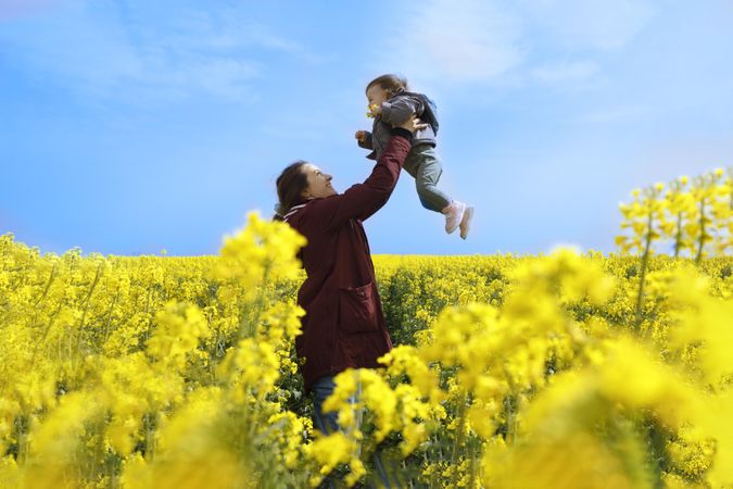 Side view of woman holding up her baby in field