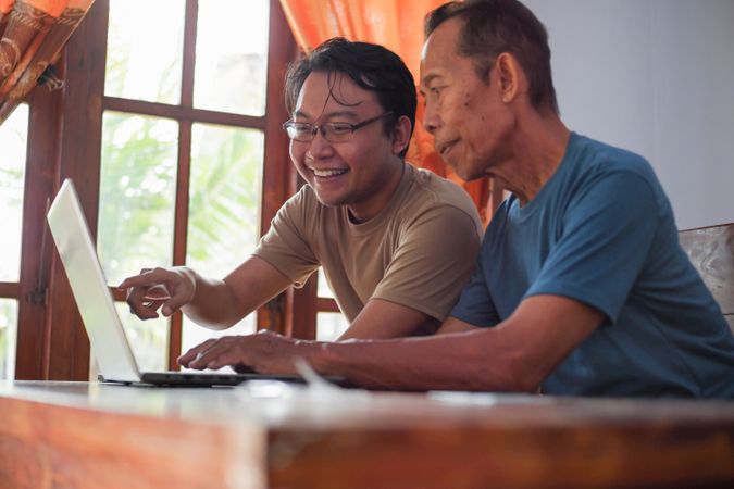 Happy adult son teaching older father using laptop