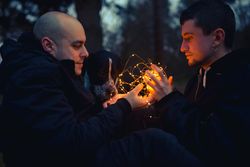 Men holding fairy lights near dog in forest at night