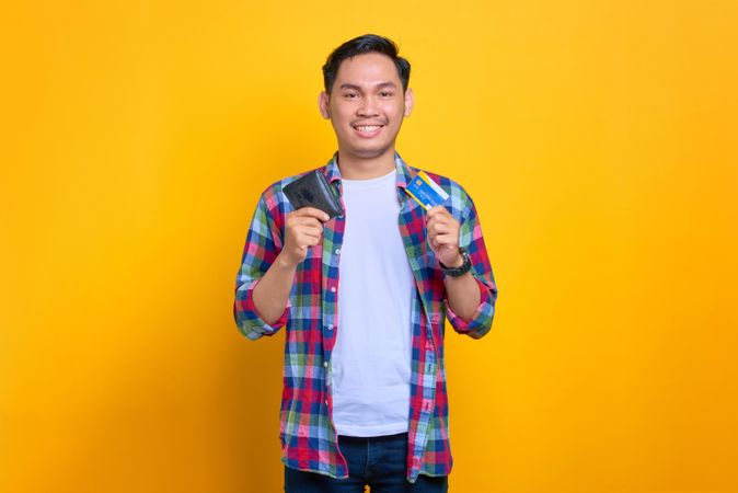 Asian man smiling while holding wallet with credit card in his other hand