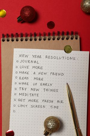 Notepad, paper with list and balls on red background, top view