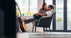 Beautiful couple looking happy while sitting together on armchair in living room 0yNQ15