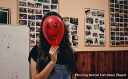 Teenage girl in dungaree hiding her face with red balloon 0P9OO5