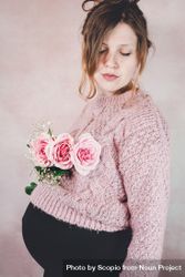 Side view of pregnant woman in knit sweater holding pink rose bouquet bDmPQ0
