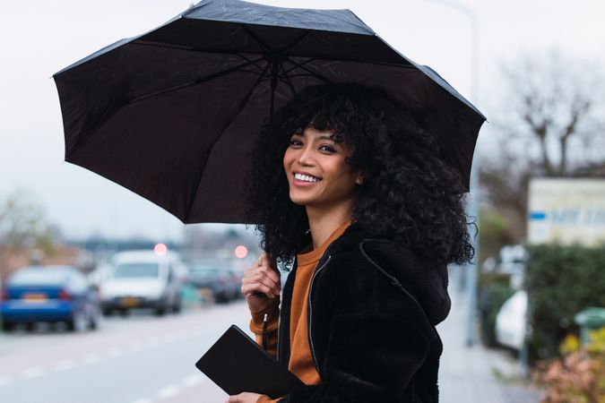 Smiling Black woman with umbrella on street