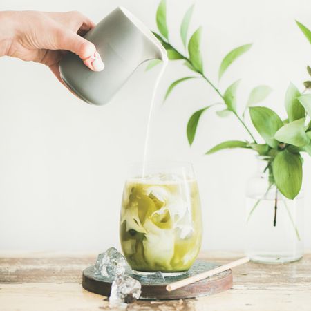 Iced matcha drink with hand pouring cream, square crop