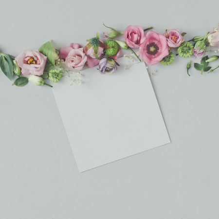 Line of pink flowers and leaves on marble background with paper card