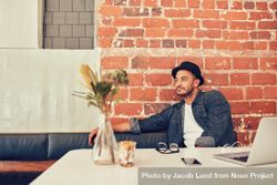 Portrait of young man wearing hat sitting alone at a cafe with laptop on table bYGqg5