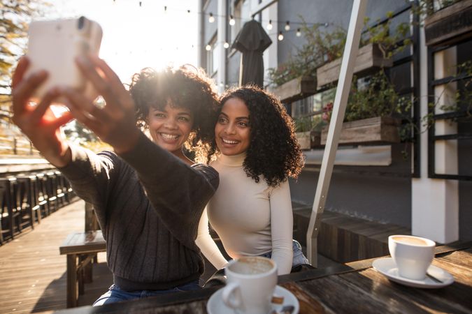 Two smiling women clicking selfie using an instant digital camera at a coffee shop