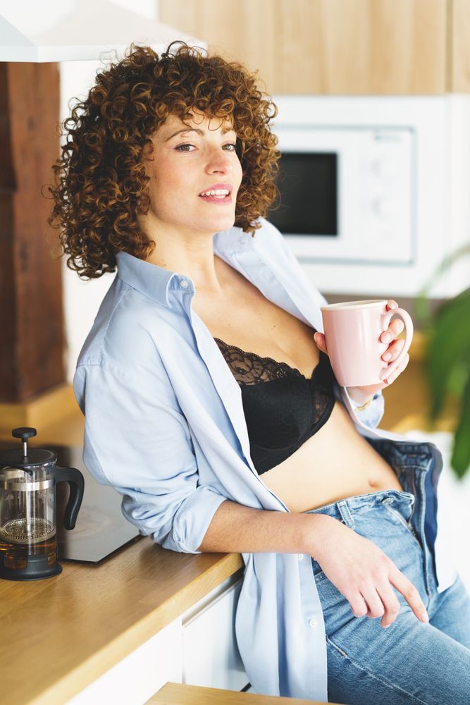 Woman relaxing in kitchen with hot drink while leaning on counter, vertical composition
