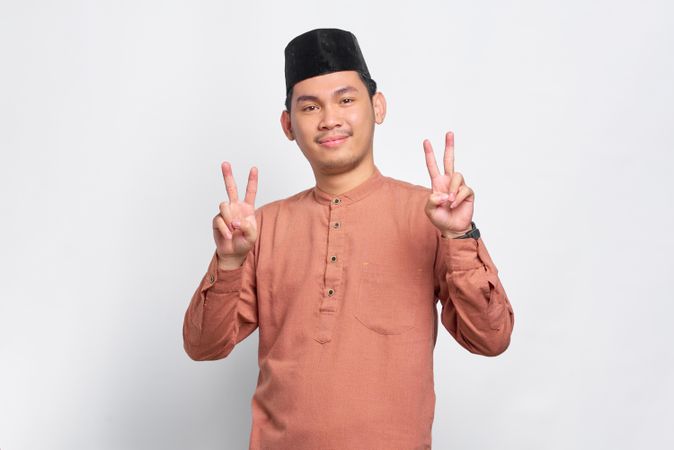Muslim man in kufi head wear with his fingers in the peace sign