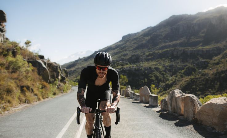 Muscular sportsman cycling outside on mountain road