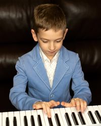 Young boy in blue blazer playing piano with focus.