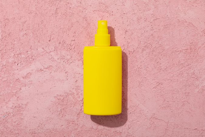 Blank sunscreen bottle on pink background, space for text