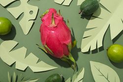 Tropical fruit and paper tropical leaves on green background, top view