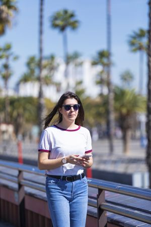 Young woman in sunglasses carrying phone on sunny day