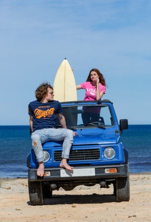 Woman with surfboard and man sitting on car