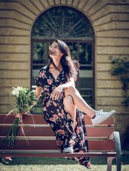 Cheerful dreamy woman sitting on back of bench with flowers