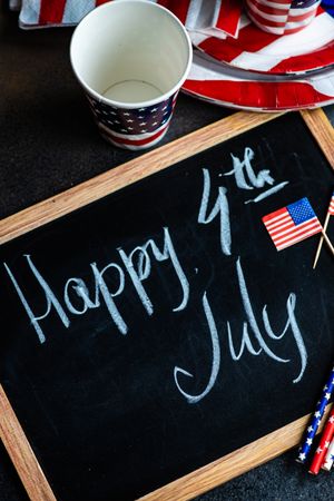 Looking down at chalkboard with the words "Happy 4th of July" with American flags and drink straws and cups