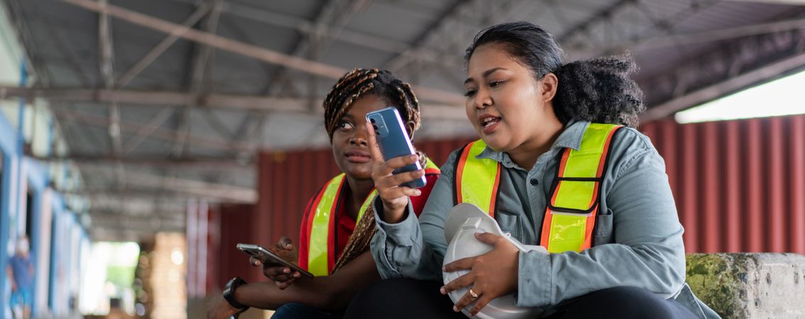 Two female workers take a break, sitting and watching on mobile phone