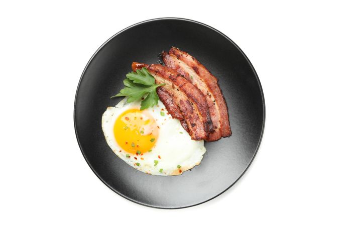 Plate with fried egg, bacon and garnish, top view