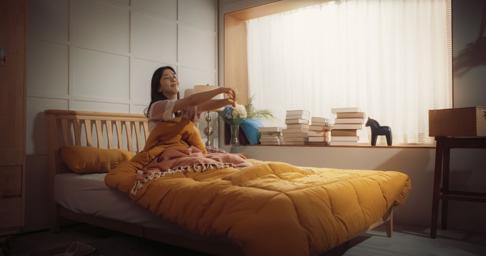 Portrait of Korean Woman Waking up in the Morning, Doing some Stretching, Sun Shines From the Apartment Window into Bedroom.