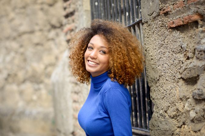 Woman with curly hair smiling in front of window with bars on street