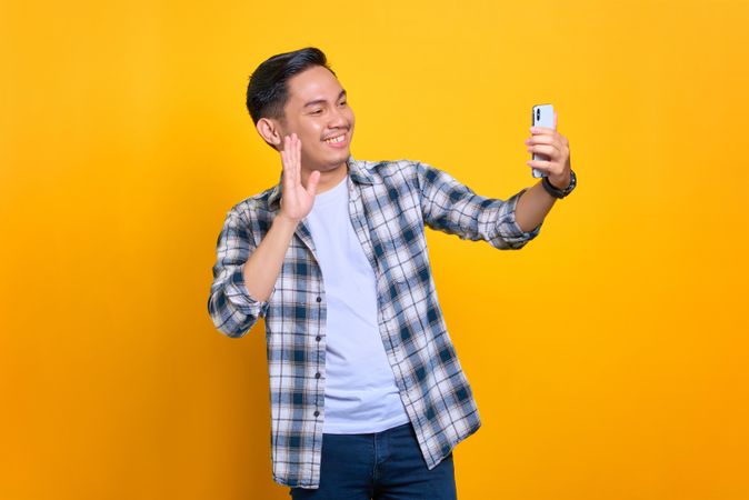 Asian male smiling while waving at his phone during video call