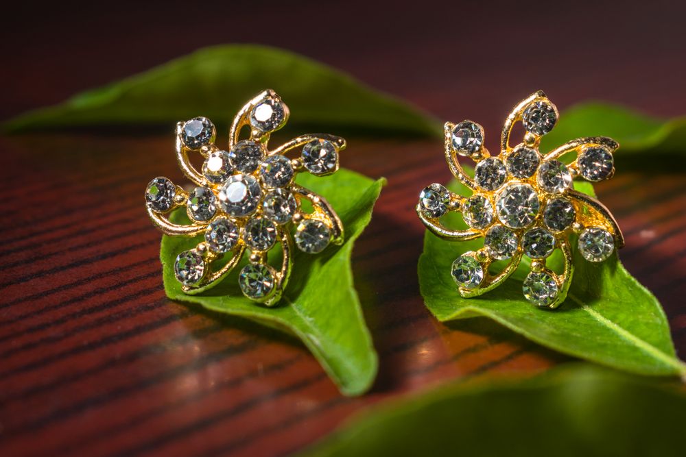 Close-up of beautiful luxury diamond earrings on green leaves with a wood background