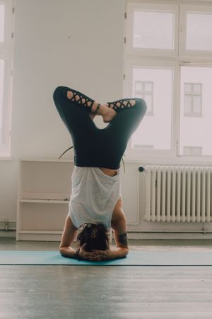 Fit woman practicing yoga pose and standing on head at home