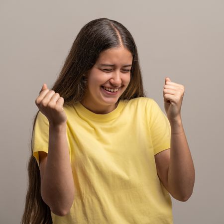 Ecstatic young woman celebrating success with clenched fists and a joyful laugh.