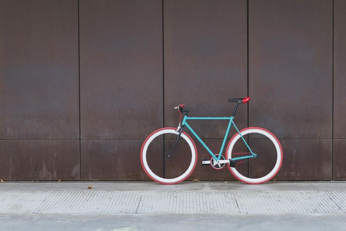 Red and green bicycle parked against a brown wall, copy space
