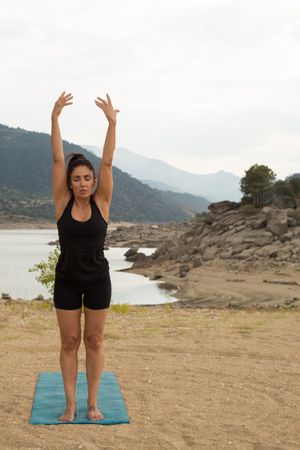 Woman practicing yoga outdoors near water
