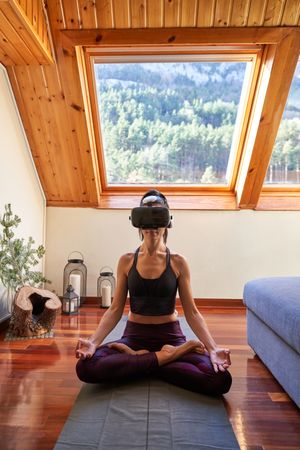 Slim woman sitting in Padmasana pose in virtual reality glasses