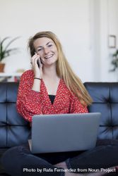 Smiling woman sitting on a sofa at home using a laptop 5Xrp6k