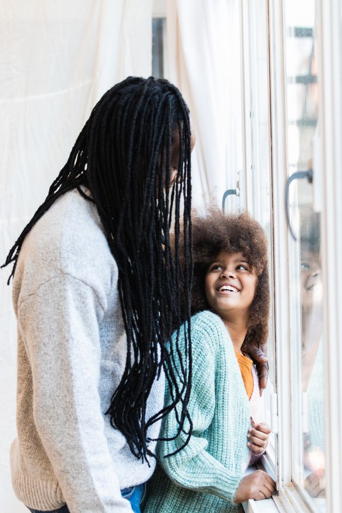 Black father with daughter standing near window