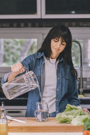 Woman pouring water in her kitchen. Vertical shot