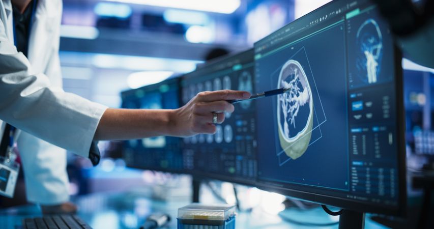 Modern Cancer Research Medical Center: Anonymous Doctor Pointing At Desktop Computer Monitor With 3D Software Visualizing Human Brain Based On CT Scan.