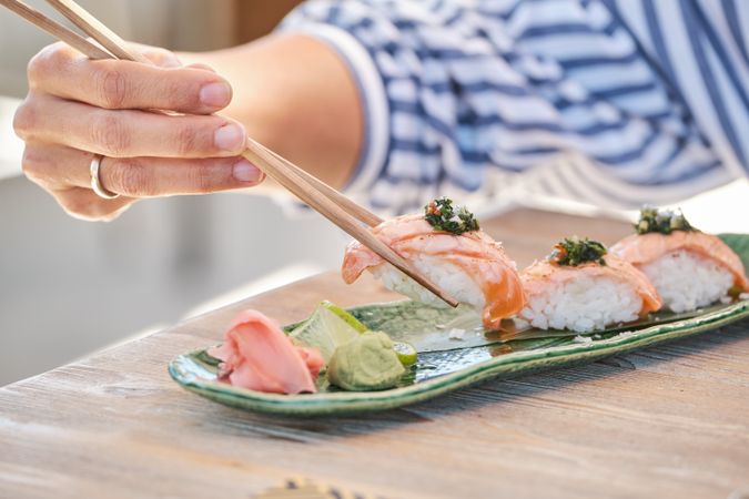 Unrecognizable woman eating sake nigiri sushi with chopsticks